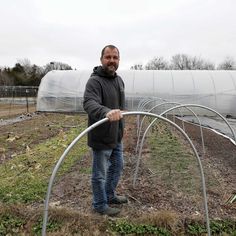 a man standing in the middle of a garden holding a hose and looking at the camera