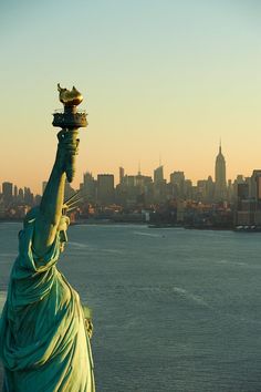 the statue of liberty stands in front of a large cityscape and looks out over the water