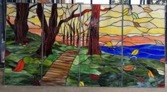 a colorful stained glass window with trees and water in the background, on a sidewalk