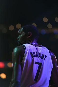 a basketball player standing in the dark with his hands on his hips and looking off into the distance