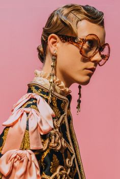 a woman wearing glasses and a dress with bows on her head is standing in front of a pink background