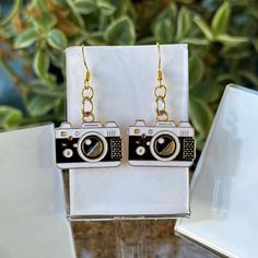 Capture the essence of nostalgia with these charming camera earrings! Featuring detailed enamel camera charms with gold accents, these earrings are perfect for photography lovers or anyone with a taste for retro accessories. The lightweight design and gold hooks make them comfortable to wear all day. **Features - Handmade with high-quality enamel and metal - Lightweight and comfortable for everyday wear - Great gift for photographers, vintage lovers, or anyone who appreciates quirky jewelry **Di Camera Earrings, Gold Hooks, Quirky Jewelry, Retro Accessories, Vintage Lovers, Gifts For Photographers, Vintage Lover, Photography Lovers, Gold Accents