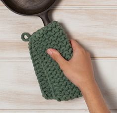 a hand holding a green knitted dishcloth next to a cast iron skillet