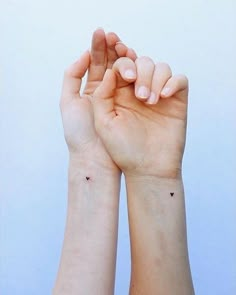 two hands holding each other with small black dots on their wrist and one hand in the air