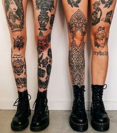 two women with tattoos on their legs standing next to each other, both wearing black combat boots