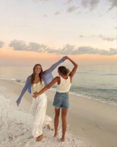 two women are dancing on the beach at sunset