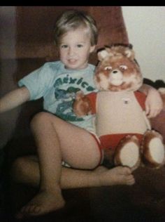 a young boy sitting on the floor holding a stuffed animal teddy bear in his lap