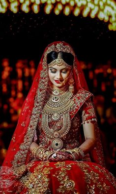 a woman in a red and gold bridal outfit sitting on the ground with lights behind her