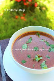 a bowl of red soup with cilantro and parsley on the side, sitting on a table outside