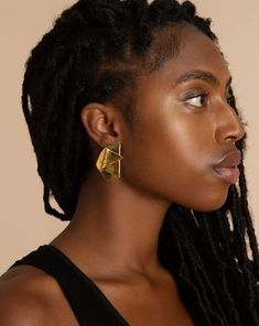 a woman with dreadlocks is looking off to the side, wearing a black top and gold earrings