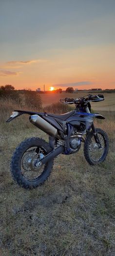 a dirt bike parked on top of a dry grass field at sunset with the sun setting in the background