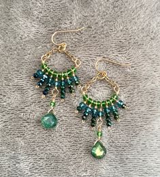 two pairs of green and blue beaded earrings sitting on top of a gray blanket