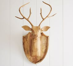 a wooden deer head mounted to the side of a white painted wall with wood planks