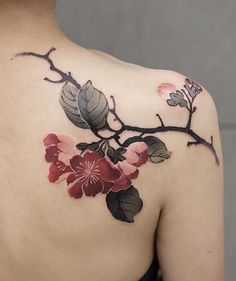 the back of a woman's shoulder with flowers and leaves tattooed on her chest