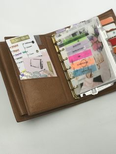 an open leather planner book with notes and pens in it on a white table top