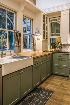 a kitchen with wooden floors and green cabinets is pictured in this image, there are two windows that look out onto the yard