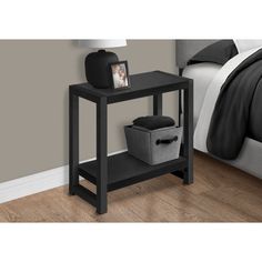 a black end table with two baskets on it and a bed in the back ground