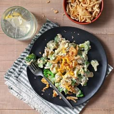 a black plate topped with pasta and broccoli next to a glass of water