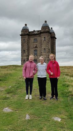 three women standing next to each other in front of a tall building on top of a hill