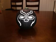 a black and white painted pumpkin sitting on top of a wooden table with chairs in the background