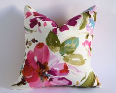 a white pillow with pink, green and purple flowers on the front is sitting against a white wall