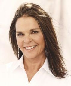 a woman with long brown hair smiling at the camera while wearing a white shirt and earrings