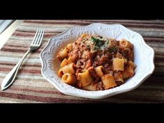 a white bowl filled with pasta and meat on top of a table next to a fork