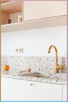 a kitchen with white cabinets and gold faucet on the counter top, next to an orange