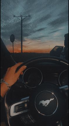 a person driving a car at sunset with the sun setting behind them and their hand on the steering wheel