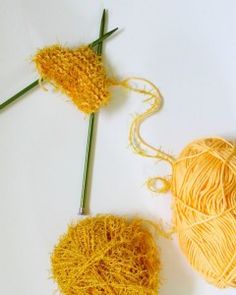 two skeins of yellow yarn next to each other on a white surface with knitting needles