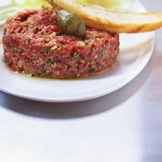 a white plate topped with meat covered in marinara sauce and an olive leaf on top of it