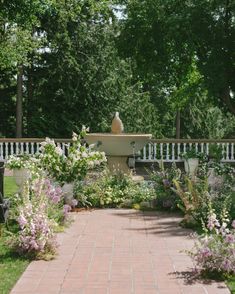 a brick walkway leads to a fountain surrounded by flowers