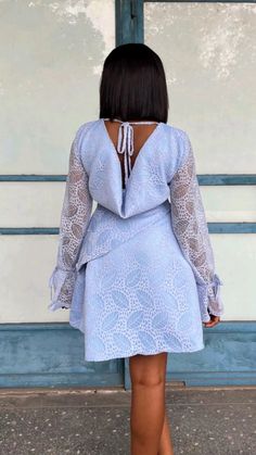 the back of a woman's blue dress with sheer sleeves and lace detailing, standing in front of a door