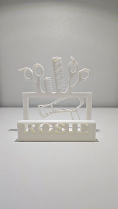 a white sculpture with scissors and combs on it's stand that says rose