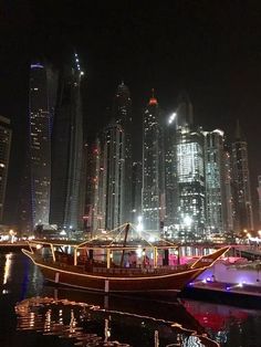 a boat floating on top of a river next to tall buildings in a city at night