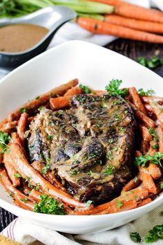 a white bowl filled with meat and carrots on top of a table next to some dipping sauce