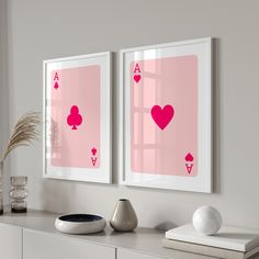 two framed pictures with pink playing cards on the wall next to a vase and potted plant