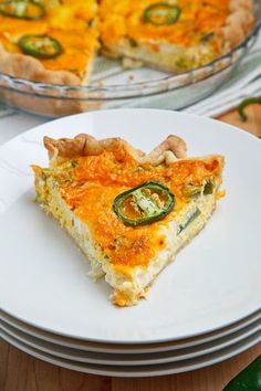 a slice of quiche on a plate next to a pie dish with green peppers