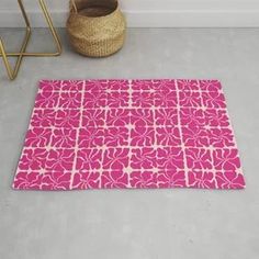 a bright pink rug with white designs on the floor next to a basket and potted plant