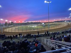 a group of people sitting on the bleachers watching a race at night time