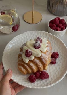 a white plate topped with a pastry covered in icing and raspberries