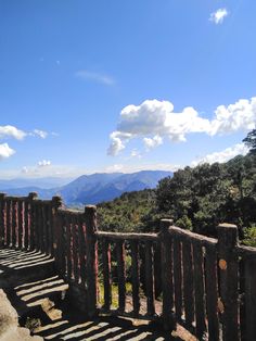 a wooden fence on top of a hill with mountains in the background and clouds in the sky