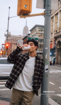 a young man drinking from a bottle next to a street sign and traffic light in the city