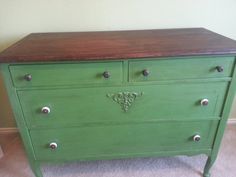 a green dresser with drawers and knobs on the bottom drawer, in front of a white wall