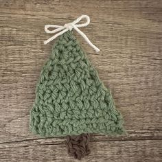 a green crocheted christmas tree ornament hanging on a wooden surface with white string