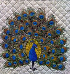 a quilted wall hanging with a blue and yellow peacock on it's side