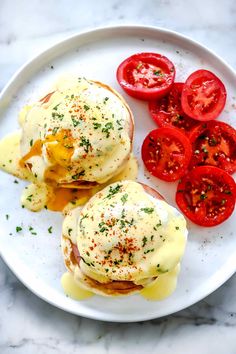 two eggs benedicts with tomatoes on a white plate