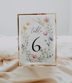 a table number with flowers on it sitting on top of a white sheet covered bed