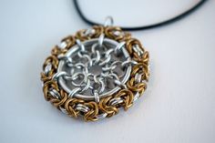 a silver and gold necklace on a black cord hanging from a white table with a gray background