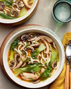 two bowls of soup with mushrooms, broccoli and noodles on a table next to utensils